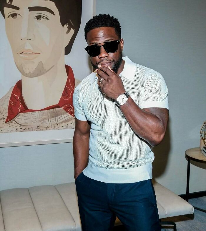 Celebrity posing indoors, wearing sunglasses and a white shirt, showcasing luxury fashion style.