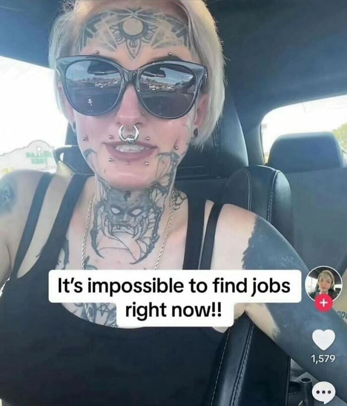 Heavily tattooed person with piercings and sunglasses, inside a car, sharing a humorous meme about job hunting challenges.