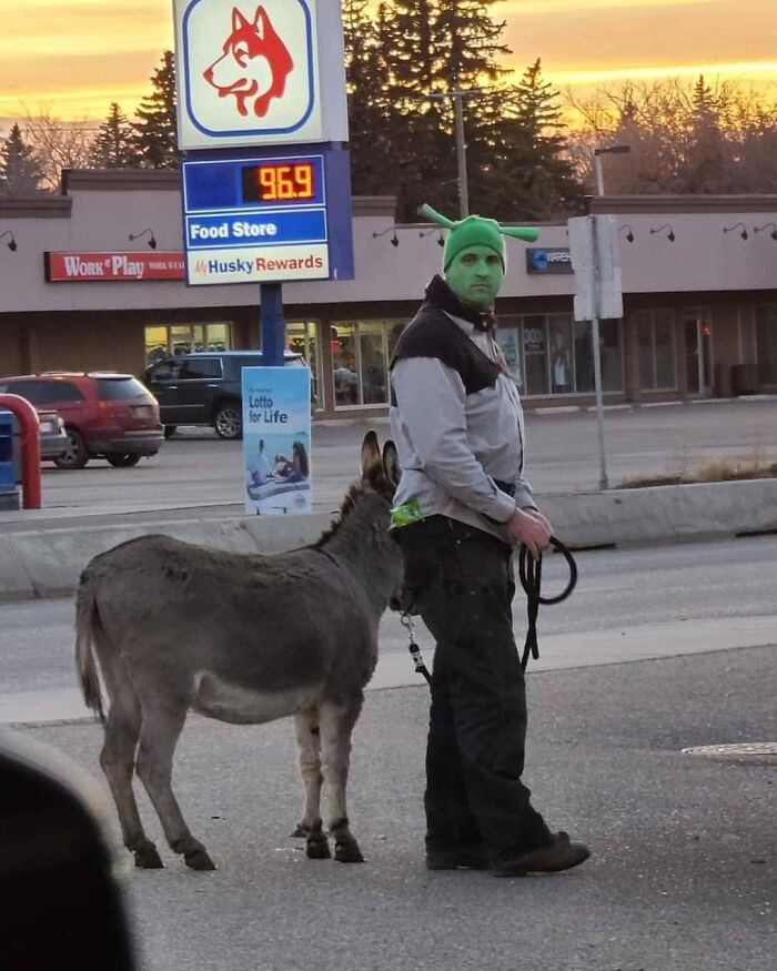 Person in green face paint walking a donkey near a gas station in Canada at sunset.
