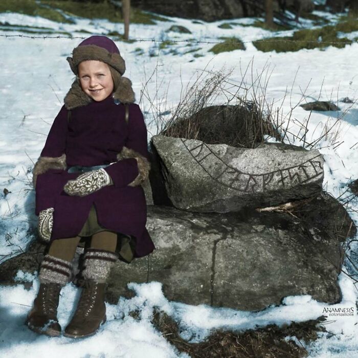 Young girl in winter clothes sits by an ancient runestone, showcasing a glimpse into historical daily life.