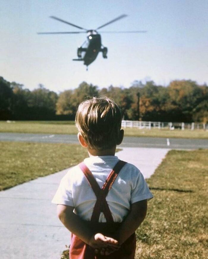 A child in red suspenders watches a helicopter fly close, capturing a moment of historical significance.