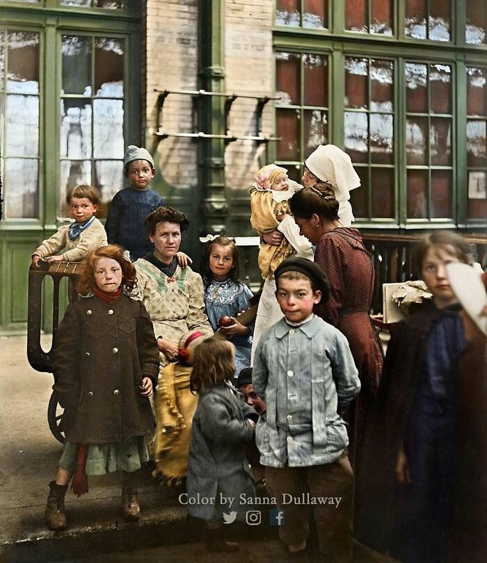 Historical image of a group of children and women dressed in early 20th-century clothing outside a building.