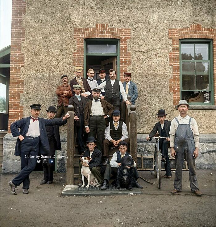 Group of historical workers posed outside a building, with bicycles and dogs, showcasing fashion and lifestyle of the past.