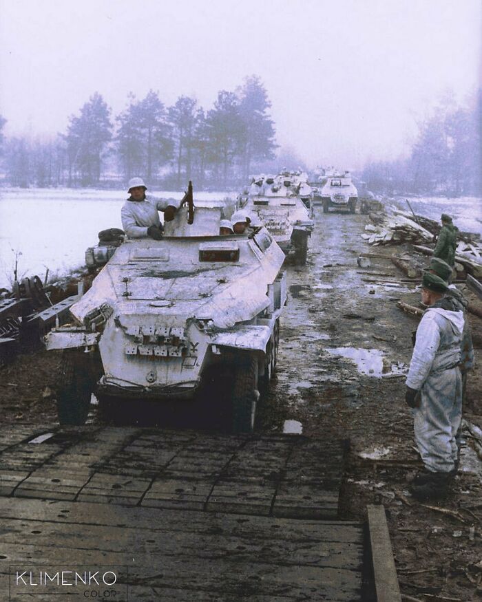 Soldiers in winter gear beside vintage armored vehicles on a muddy road, portraying a historical moment from the past.