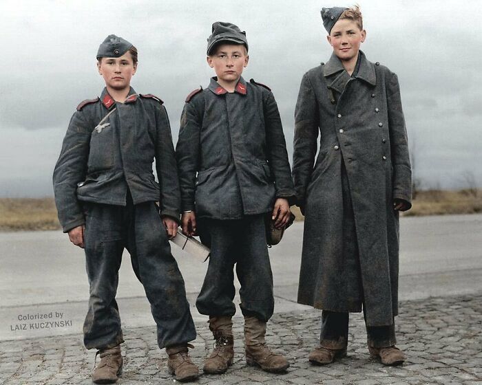 Three young soldiers in historical uniforms, standing on a road, representing a moment from the past.