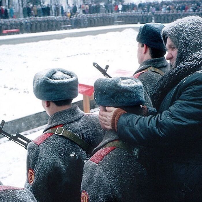 Soldiers in winter uniforms, covered in snow, with an observer standing behind them. Historical scene with significant past context.