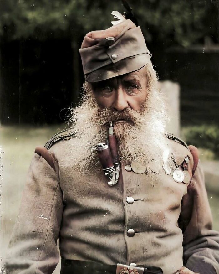 Historical photograph of an elderly man in military attire with medals and a pipe, reflecting past eras.