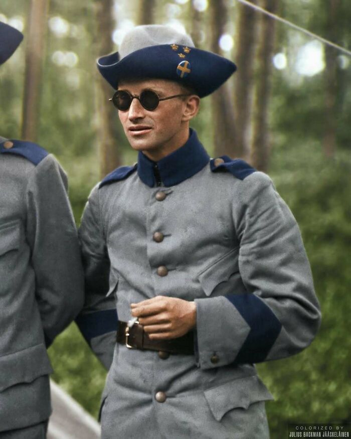 A historical image of a man in period military attire and sunglasses, set in a wooded area.