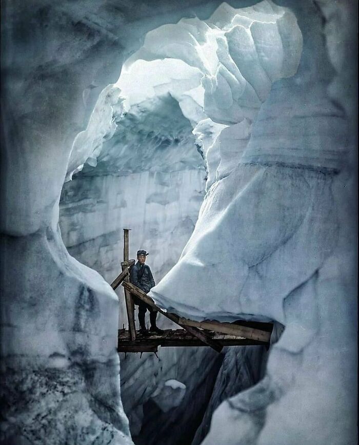 A climber stands on a wooden bridge over an ice crevasse, showcasing a historical moment in exploration.