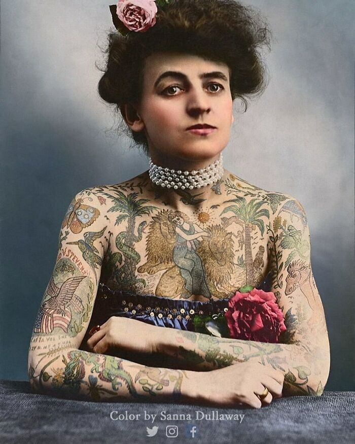 A historical portrait of a woman with extensive tattoos and a floral accessory, highlighting past tattoo artistry.