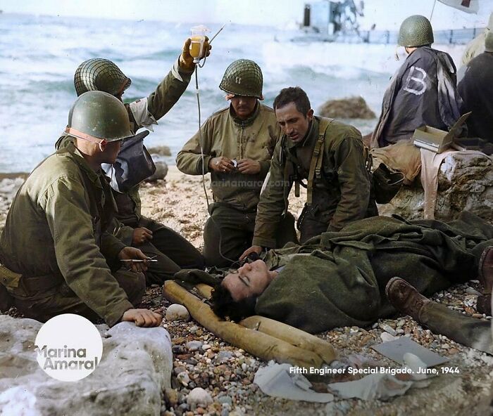Soldiers on a beach aiding a wounded comrade, showcasing a vivid historical moment from the past.