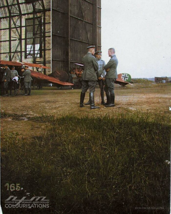 German soldiers in front of vintage aircraft, discussing events, showcasing historical aviation moments.