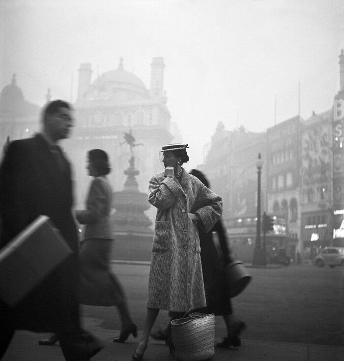 Vintage street scene with a stylish woman in a coat and hat, evoking historical nostalgia in a foggy city setting.