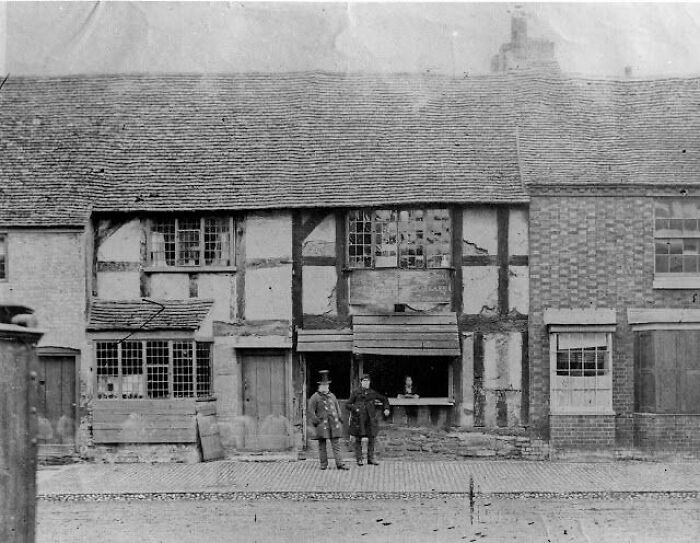 Historical photo of two men standing in front of an old timber-framed building, capturing a sense of nostalgia.