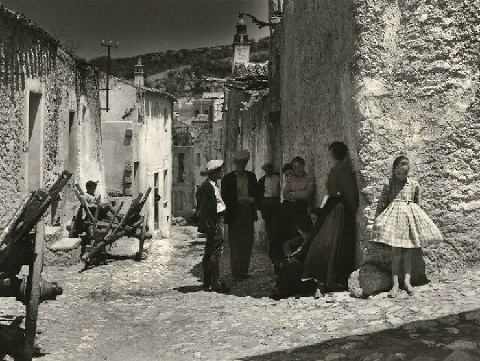 Historical pic of people in a cobblestone street, creating a nostalgic scene with old stone buildings and rugged cartwheels.