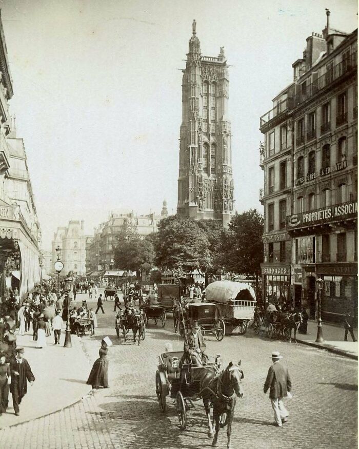 Historical street scene with horse-drawn carriages and a large tower, evoking nostalgia.
