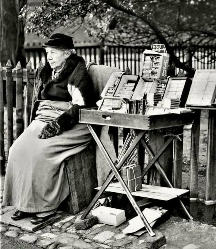 Elderly woman selling postcards at a vintage street stall, capturing historical nostalgia.