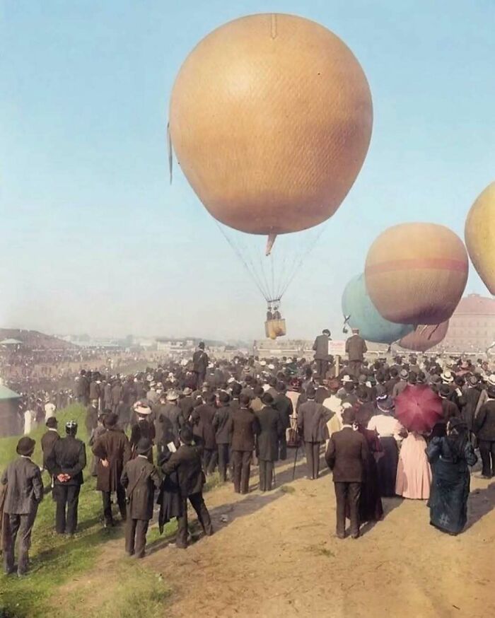 Historical pic of a crowd watching hot air balloons taking off, evoking nostalgia with vintage fashion and scenery.