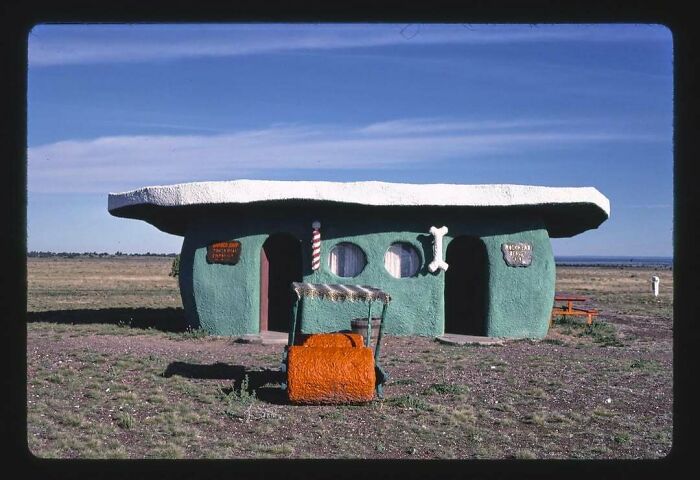 Retro building resembling a cartoon house with a stone-age car in front, evoking nostalgia in a vast open field.