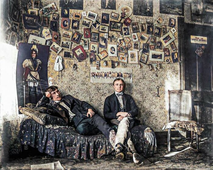 Two young men in a vintage room with historical photos on the wall, evoking nostalgia and a glimpse into the past.