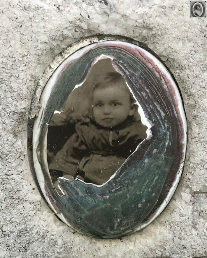 Vintage headstone portrait of a baby in an oval frame, set in a weathered stone surface.
