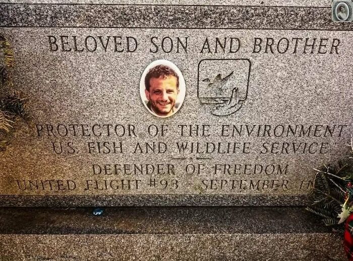 Headstone portrait of a smiling man, with inscriptions honoring him as a son, brother, and environmental protector.