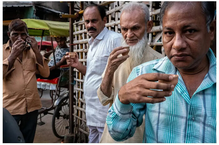 Four men drinking tea stand on a bustling street, captured in a raw, unfiltered moment by Andrés Ramos.