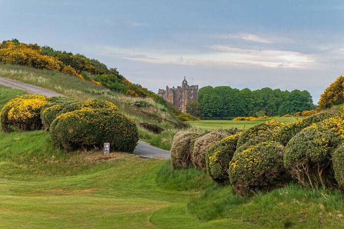Breathtaking golf course with lush greenery and a distant castle, popular among golfers traveling globally for a unique round.