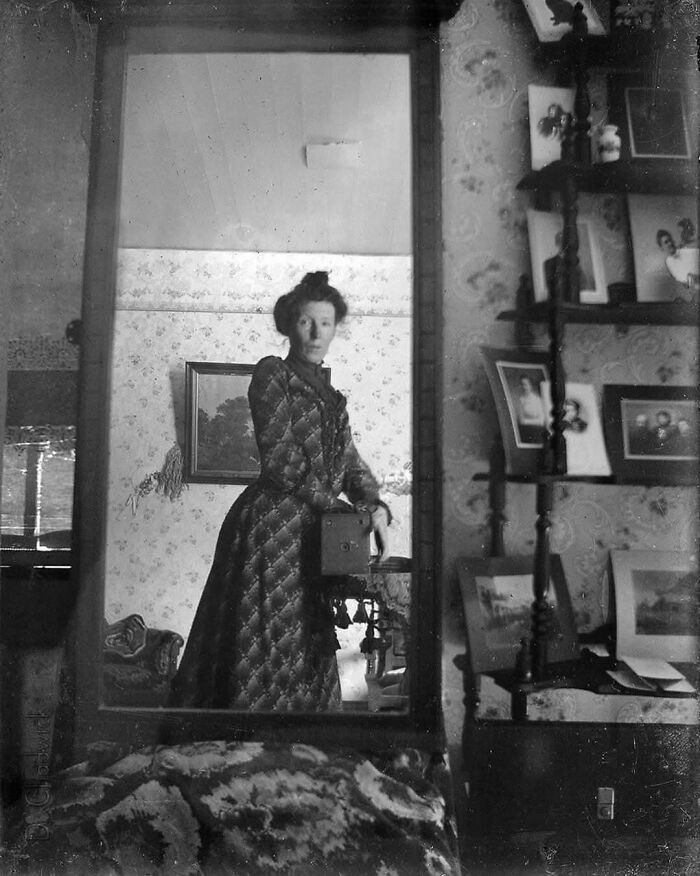 Victorian woman taking a mirror selfie with an old camera, surrounded by nostalgic decor and photographs.