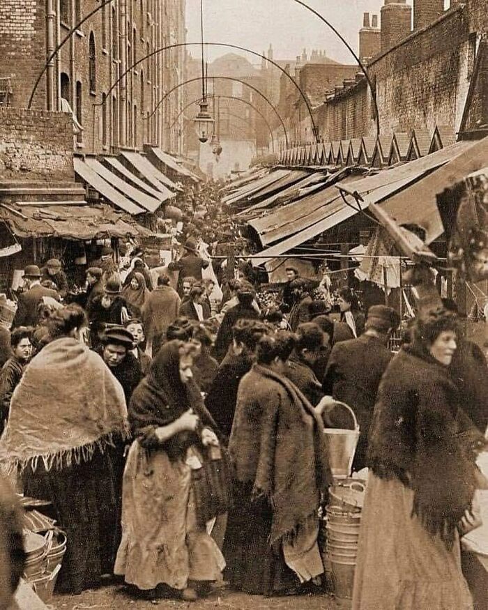 Crowded historical street market with people in period clothing, adding nostalgia through a sepia-toned scene.