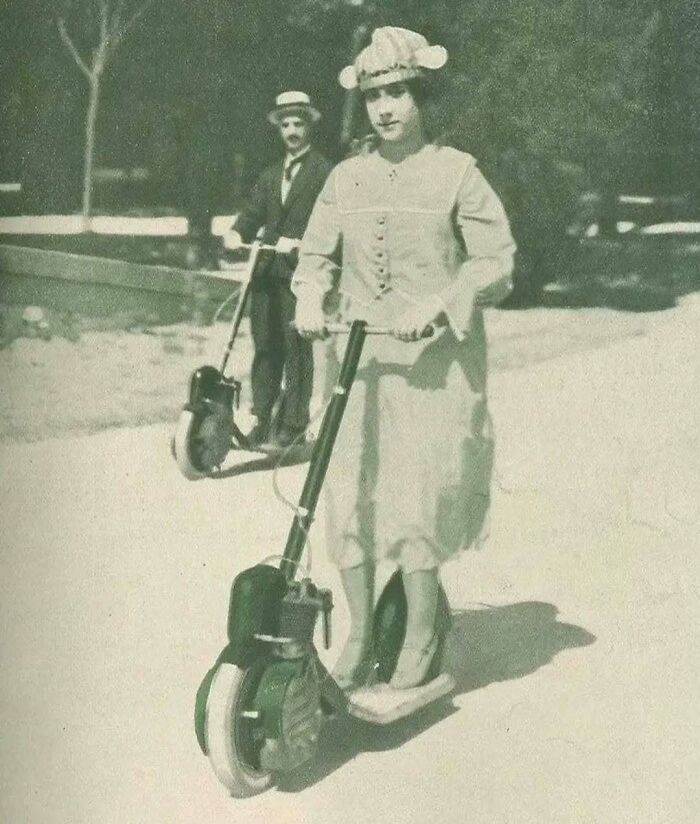 Vintage scene with two people riding early motorized scooters, adding nostalgia to the day.
