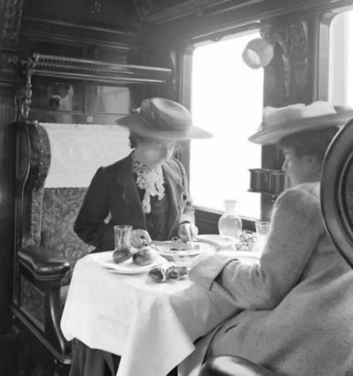 Two women in vintage attire dining in a historical train carriage, evoking nostalgia.