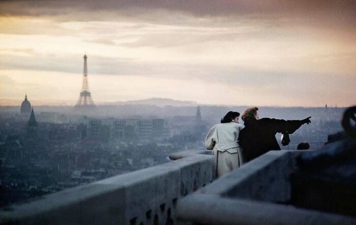 Two people on a Paris rooftop at dusk, pointing towards the Eiffel Tower, evoking nostalgia with historical charm.