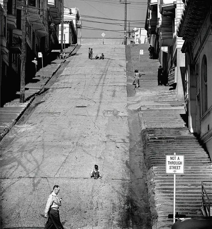Steep historical street scene with children and adults, capturing a nostalgic moment of urban life in black and white.