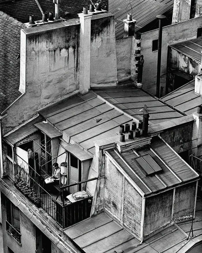 Black and white historical rooftop scene with a person reading, evoking nostalgia.