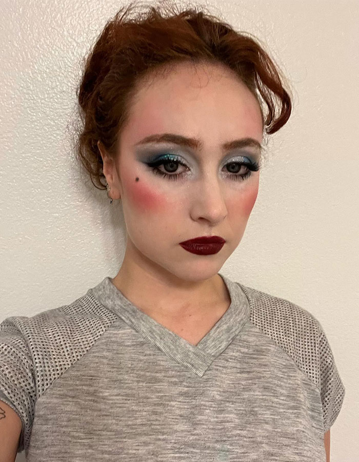 Young woman with bold makeup and a subtle expression, wearing a grey shirt; a look inspired by Paris Fashion Week debut.