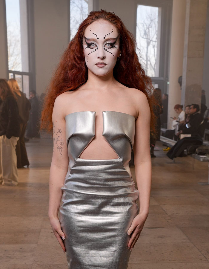 Fashion Week debut look with futuristic silver dress and bold makeup.