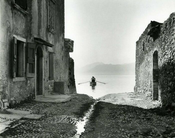 Rowboat on calm water between historical stone buildings.