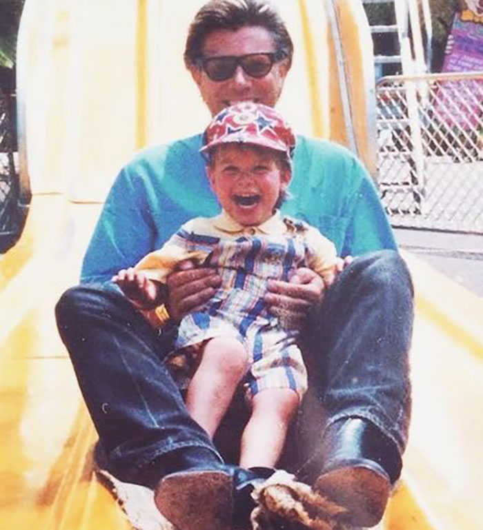 Father and son enjoying a slide ride at a park, showcasing a joyful moment.