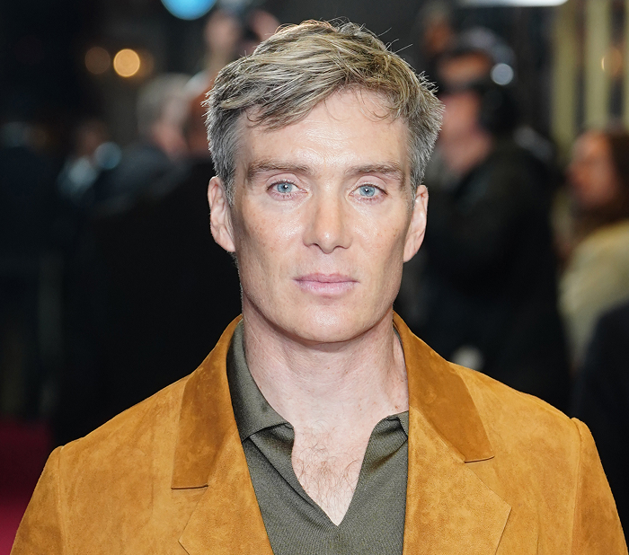 A celebrity in a brown suede jacket at an event, showcasing a more attractive look in person than on screen.