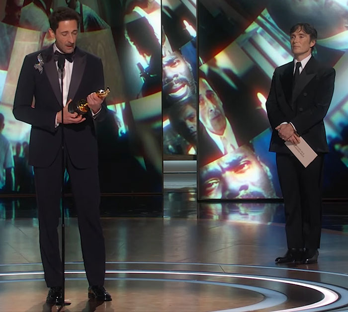 Adrien Brody giving Oscars speech while another man stands nearby, scene goes viral.
