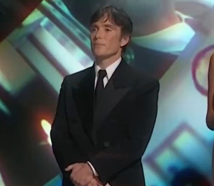 Man in a tuxedo standing during the Oscars, looking composed, related to viral Oscars speech moment.
