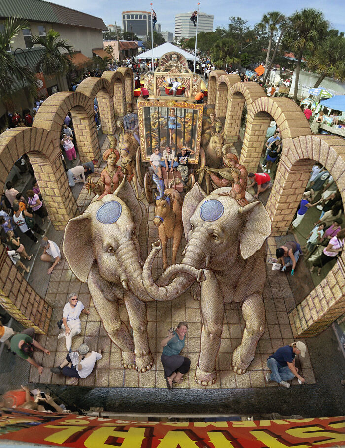 3D street art masterpiece with elephants and Roman chariot, surrounded by onlookers in a busy outdoor setting.