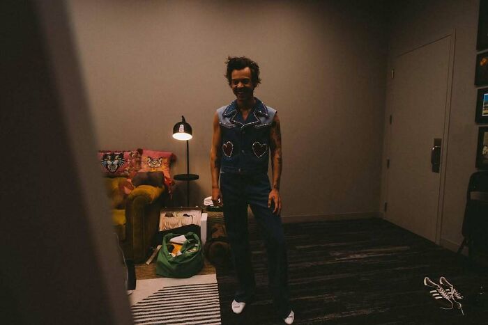 Man in a denim outfit standing in a dimly lit room with eclectic decor, representing a take on attractive celebrities.