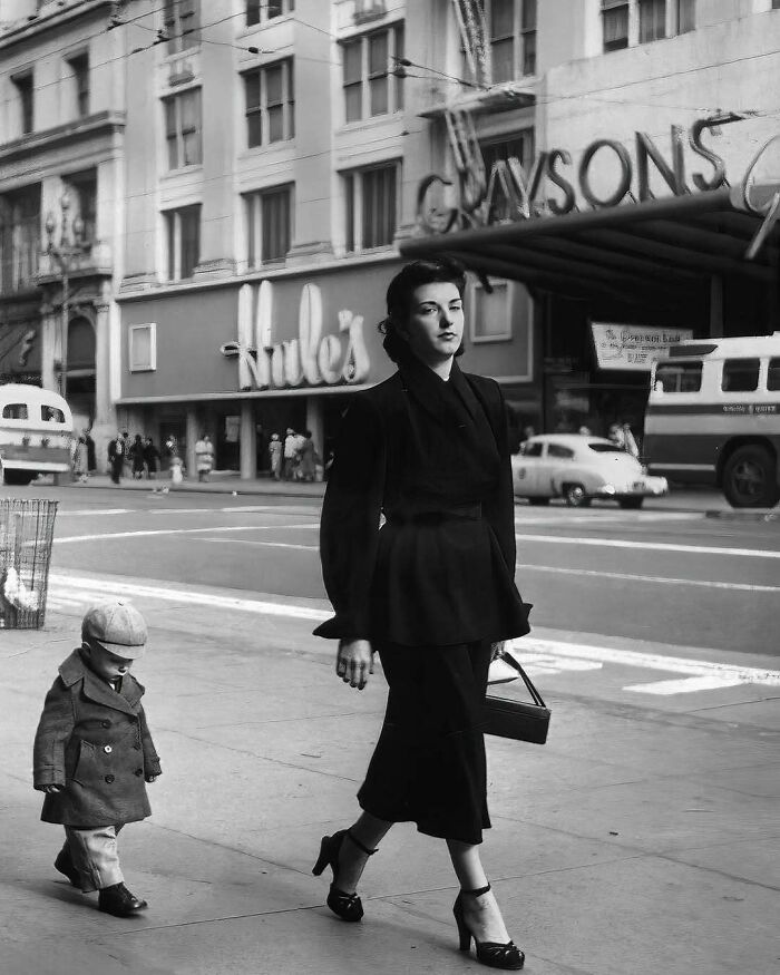 Woman and child in vintage attire walking on a city street, evoking historical nostalgia.