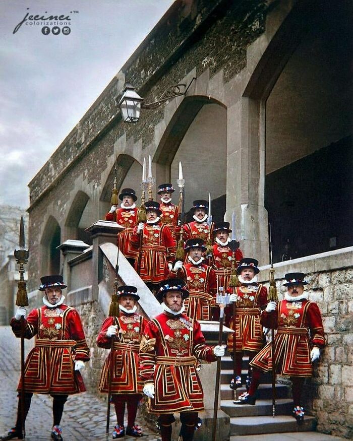 Beefeaters in ceremonial uniforms, standing on stone steps, representing historical British tradition.