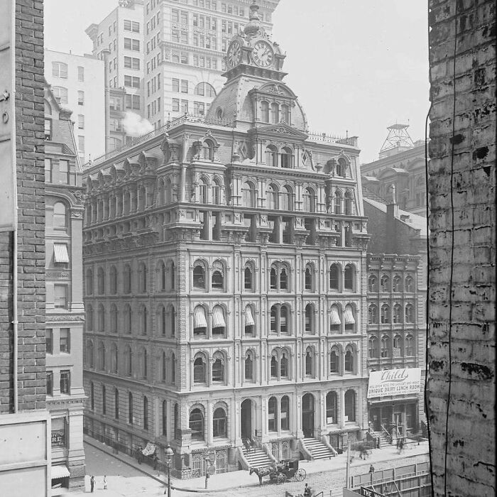 Old American architecture featuring an ornate multi-story building with a clock tower, surrounded by city structures.