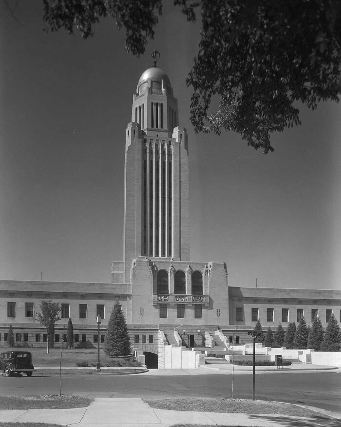 Art Deco-style tower of historical American architecture, with trees and vintage car in the foreground.