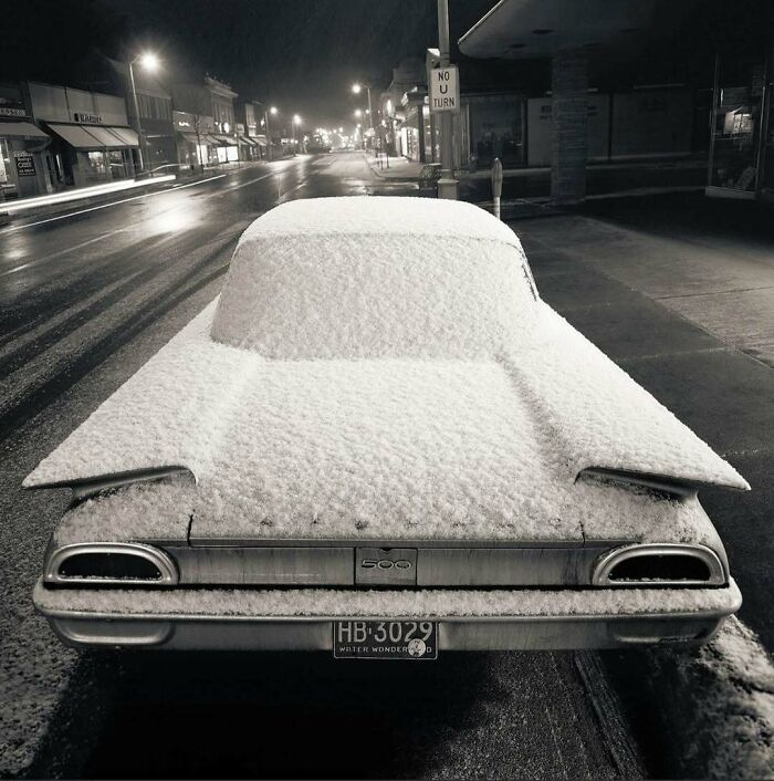 Vintage car covered in snow on a quiet street, evoking nostalgia with its historical charm.