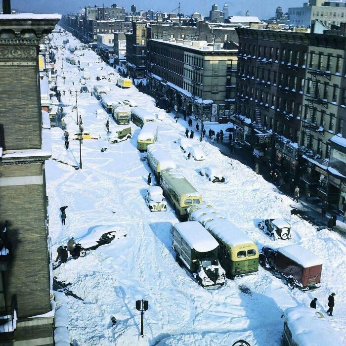 Historical city street blanketed in snow, with vintage buses and cars partially buried, evoking nostalgia.